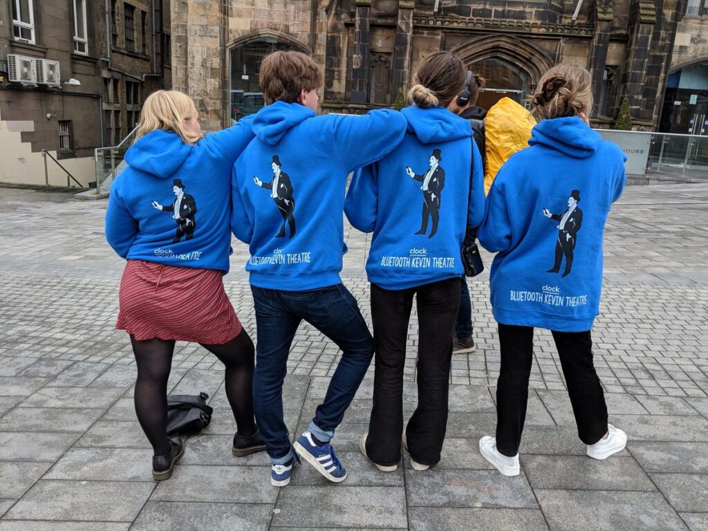 Line of four Bluetooth Kevin Theatre members showing off the backs of their hoodies.