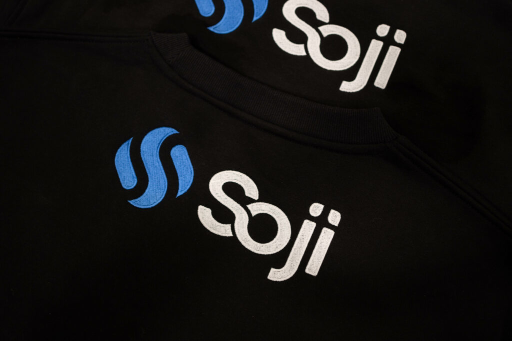 A stack of sweaters with the Soji logo on the top back.