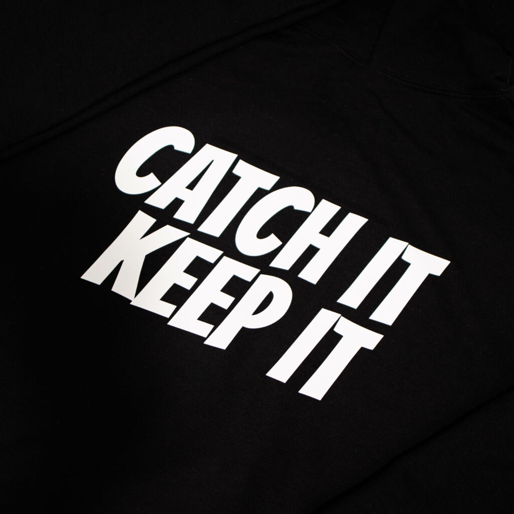 Logo that reads 'CATCH IT KEEP IT' on the back of a folded hoodie.